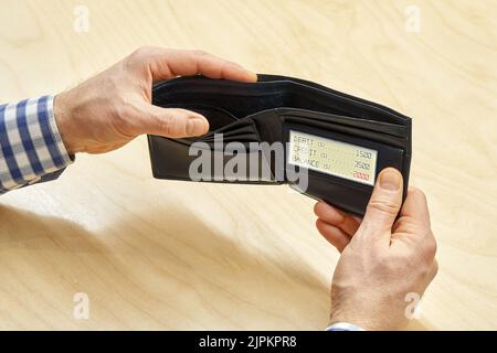 Les mains de l'homme tiennent un portefeuille noir vide avec écran électronique affichant un solde négatif à la table. Le concept de pauvreté et de crise est un gros plan Banque D'Images