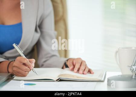 Image rognée de la femme busienss écrivant des plans pour la semaine prochaine dans son bloc-notes Banque D'Images