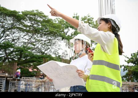 Une femme femme d'ingénieur civil asiatique professionnelle du millénaire explique un processus de construction à une femme architecte lors d'une inspection du chantier de construction. Banque D'Images