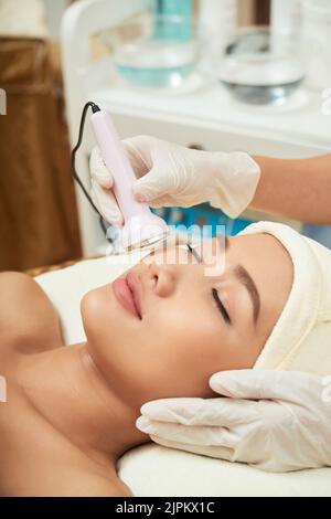 Gros plan d'une jeune femme vietnamienne couché sur une table de traitement avec les yeux fermés pendant une procédure de resurfaçage de la peau dans la salle du visage Banque D'Images