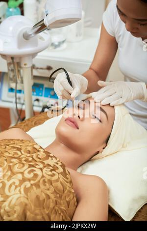 Jolie femme vietnamienne ayant un soin de la peau tout en passant une journée dans la salle du visage moderne, gros plan Banque D'Images