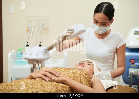 Cosmetologiste vietnamien hautement professionnel portant des gants en caoutchouc et un masque médical debout à la table de traitement et faisant les préparations nécessaires pour la procédure de beauté Banque D'Images