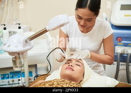 Belle femme asiatique couchée sur une table de traitement et d'obtenir la thérapie au laser dans le salon de spa moderne, une esthéticienne hautement professionnelle enveloppée dans le travail Banque D'Images