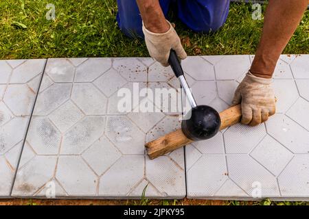 Le maître pose les pavés en couches. Pavage de chemins de briques de jardin. Pose de dalles de béton dans la cour de la maison sur une base de sable Banque D'Images