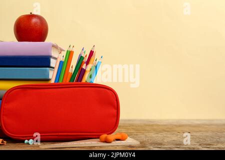 Étui à crayons rouge avec papeterie scolaire et pomme sur table sur fond beige Banque D'Images