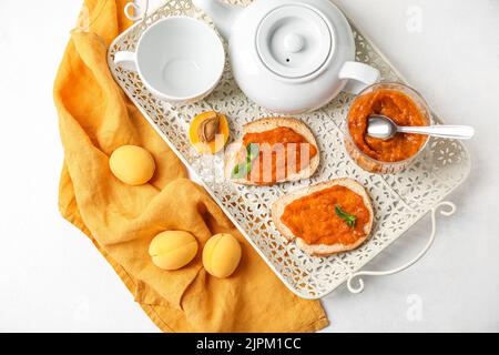 Plateau avec sandwiches savoureux, confiture d'abricot et thé sur fond clair Banque D'Images