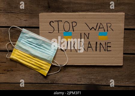 Les masques médicaux, jaunes et bleus, comme le drapeau de l'Ukraine, se trouvent sur une table en bois et un signe avec le texte arrête la guerre en Ukraine. Drapeau d'Etat d'Ukrain Banque D'Images