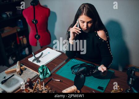 Tanner femme faisant le harnais en cuir et appeler le téléphone mobile client à l'atelier. Processus de travail de l'artisan du cuir. Banque D'Images