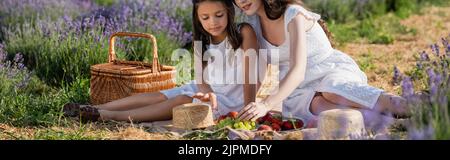 fille et maman assis près du panier de paille et des fruits frais pendant le pique-nique dans la prairie, bannière Banque D'Images