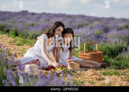 mère et enfant assis dans le champ près des fruits frais et du panier de paille Banque D'Images