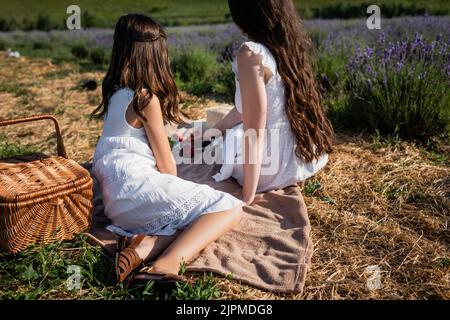 vue arrière de la femme et de la fille brunette dans des robes blanches assis sur une couverture dans le champ Banque D'Images