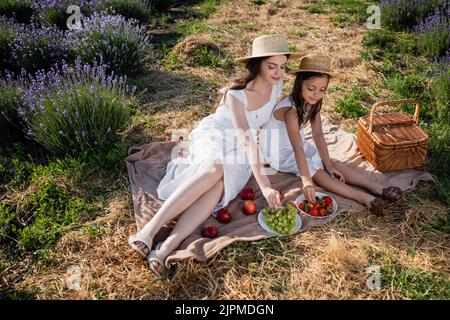 vue en grand angle de la mère et de la fille mangeant des fruits dans le champ de floraison Banque D'Images