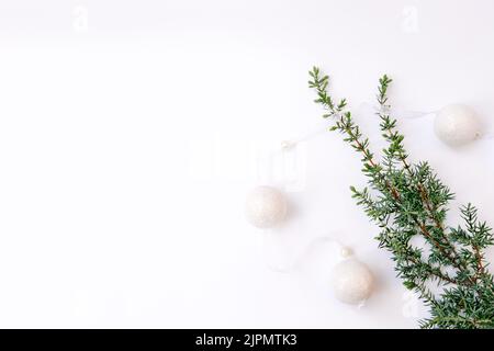 Guirlande blanche. La décoration du nouvel an et une branche d'un arbre de Noël ou d'un genévrier sur un fond blanc dans un coin de la photo. Balles rondes avec ruban. Pose à plat. Copier l'espace. Mise au point sélective douce. Banque D'Images