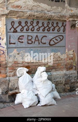 Belgrade-Serbie - 15 juin 2022: Détail de la vieille maison en ruines avec graffiti 'pain' sur un mur de façade et constructeurs de sacs à ordures en vrac Banque D'Images