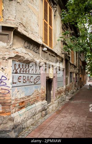 Belgrade-Serbie - 15 juin 2022: Ancienne maison ruinée avec des graffitis 'pain' et un dessin de lui sur un mur de façade dans une rue assez vide dans Dorcol Banque D'Images