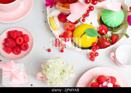 Sucreries roses et blanches et fruits rouges, desserts aux fruits sur un présentoir à gâteaux, théière sur table blanche dans un magasin de bonbons, café. Vue de dessus Banque D'Images