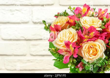 Bouquet de belles roses et alstroemeria sur fond de briques blanches. Un bouquet frais et luxuriant de fleurs colorées pour le mariage, le jour de la fête des femmes, le jour de la fête des mères Banque D'Images