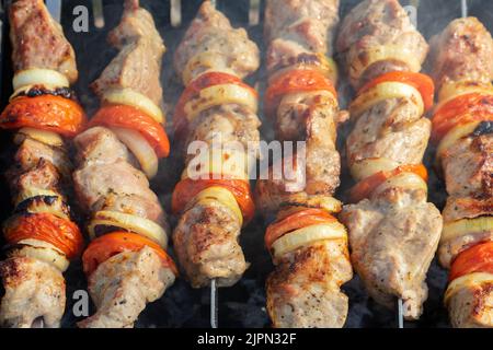 Barbecue viande de kebabs de porc grillée, morceaux de viande sur brochettes. Processus de cuisson de viande marinée avec épices et tomate. Pique-nique extérieur, barbecue Banque D'Images