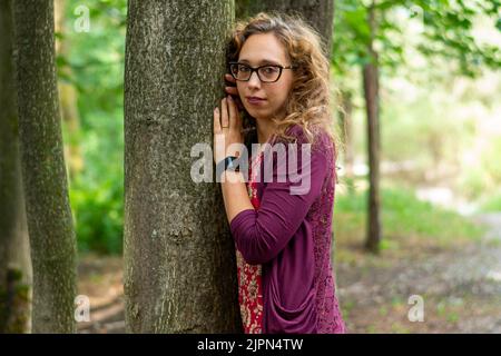 Femme blonde avec des lunettes penchées vers un arbre Banque D'Images