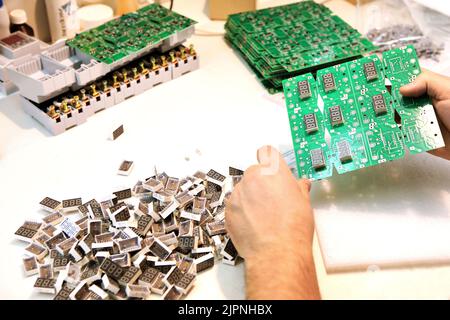 Un homme collecte une carte de circuit imprimé. Le travailleur souéquipe les composants de la radio et assemble le dispositif fini. Montage et commande manuels Banque D'Images