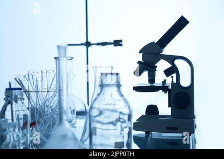 Banc de laboratoire avec microscope moderne, tubes à essai, flacons et flacons en verre, fond blanc Banque D'Images