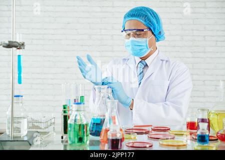 Portrait à la taille haute d'un scientifique hautement professionnel portant des gants en caoutchouc à revêtement blanc réglable tout en étant debout sur une paillasse de laboratoire Banque D'Images