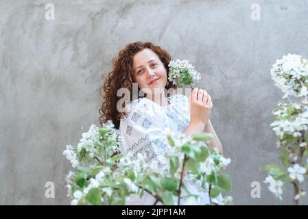 Femme long cheveux bouclés en blanc brodé Ukraine chemise. Accent défoqué sur le premier plan sur les branches en fleur de pommier sur le fond du contre Banque D'Images