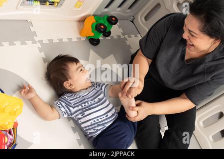 bébé garçon de 11 mois à la maison interaction ludique avec la mère, en riant alors qu'elle tickle son pied Banque D'Images