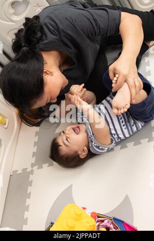 bébé garçon de 11 mois à la maison avec mère, interagissant, jouer physique, rire Banque D'Images