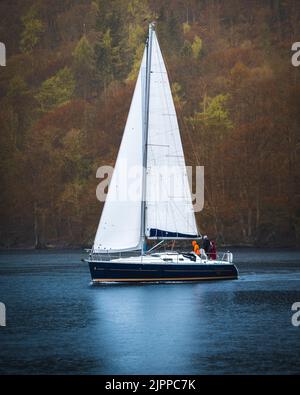 Un voilier avec de grands voiles blanches naviguant sur un lac près des arbres d'automne Banque D'Images