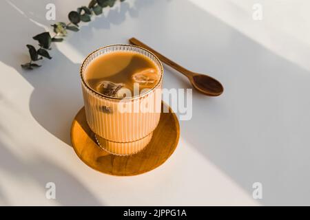Café avec glace dans un verre de cristal sur la table blanche dans la lumière naturelle, de longues ombres Banque D'Images