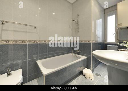 Salle de bains avec lavabo sur pied en porcelaine assorti, baignoire d'angle, carrelage bleu et blanc avec bordure décorative Banque D'Images