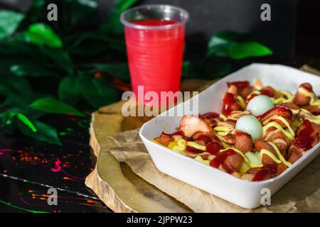 cuisine de rue colombienne, salchipapa servi sur un plateau en bois avec un verre de jus de fruits rouges à côté. restauration rapide avec pommes de terre, saucisses, œufs et sauces. Banque D'Images