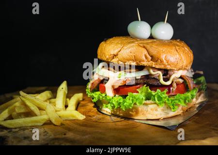 hamburger colombien avec pommes de terre, servi sur un plateau en bois en forme de tronc d'arbre. hamburger avec deux œufs de caille sur le dessus imitant les yeux. rue f Banque D'Images