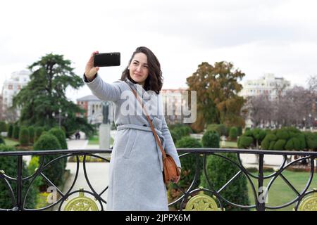 Jeune femme élégante visite. Elle prend une photo avec son téléphone mobile dans un jardin de ville. Espace pour le texte. Banque D'Images