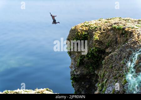 Photo en grand angle d'un homme qui saute d'une falaise en vacances Banque D'Images
