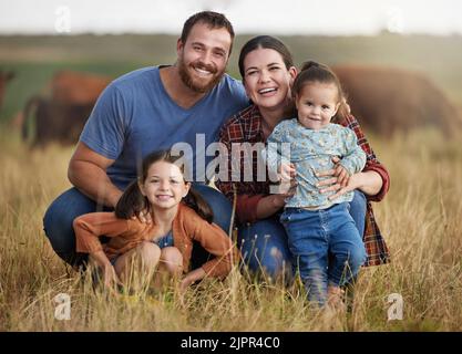 Portrait d'une famille heureuse sur un champ de ferme de campagne avec des vaches en arrière-plan. Les parents d'agriculteurs se sont solidaires avec les enfants sur un bétail agricole durable Banque D'Images