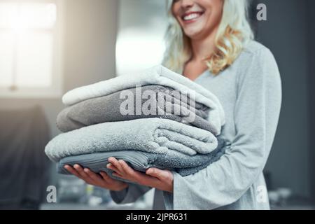 Une pile de linge frais arrive. Gros plan d'une femme méconnue portant un tas de serviettes tout en faisant du linge à la maison. Banque D'Images