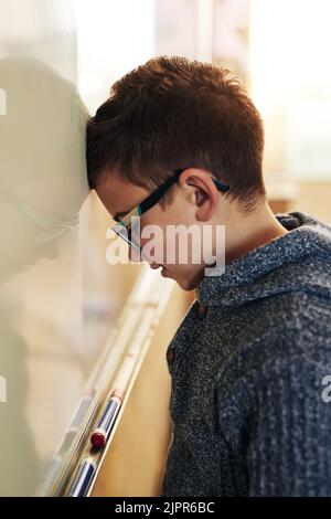 HES réfléchit dur à la réponse : un garçon de l'école élémentaire se penchait avec sa tête sur le tableau blanc en classe. Banque D'Images