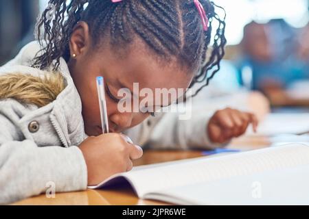 Axé sur la tâche que l'enseignante ou l'enseignant a donnée, une jeune fille d'école élémentaire qui fait du travail à l'école en classe. Banque D'Images