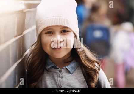 Souriant jusqu'à sa prochaine classe. Portrait d'une jeune fille d'une école primaire debout dans le couloir de l'école. Banque D'Images