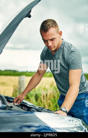 Maintenant, d'où vient ce bruit étrange... un jeune homme qui vérifie sous le capot de sa voiture après s'être arrêté sur la route. Banque D'Images