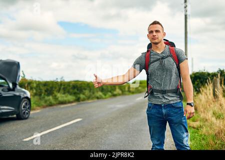 Un jeune homme se déplace au lieu d'être laissé coincé. Un jeune homme s'en marche après avoir eu des problèmes avec sa voiture sur la route. Banque D'Images