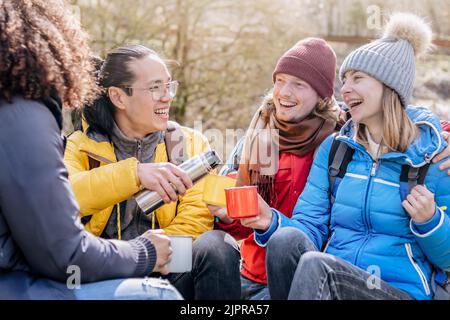 Groupe multiculturel de randonneurs assis sur le dessus de la montagne buvant un café avec des sacs à dos - heureux amis hippster ayant trekking journée ensemble - Banque D'Images