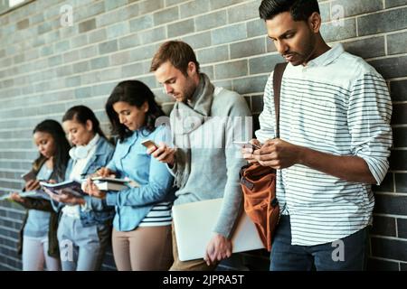 Relié sur le campus. Groupe d'étudiants universitaires utilisant leur téléphone cellulaire dans un couloir du campus. Banque D'Images