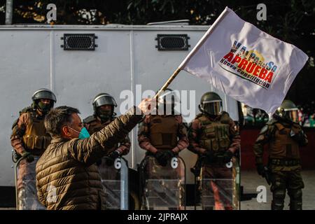 Valparaiso, Chili. 19th août 2022. Un contre-manifestant lève un drapeau pour l'approbation d'une nouvelle constitution alors que la police garde en arrière-plan pendant la manifestation. Des manifestants s'empaissent dans les rues de Valparaiso pour rejeter une nouvelle constitution, certains contre-manifestants soutenant la nouvelle constitution de Valparaiso. Crédit : SOPA Images Limited/Alamy Live News Banque D'Images