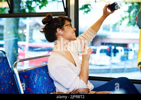 Un pour la route. Une jeune femme attrayante prenant des selfies avec son smartphone tout en étant assise dans un bus. Banque D'Images