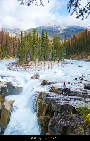 Sunwapta Falls Parc national Jasper, Canada. Les Rocheuses canadiennes pendant la saison d'automne. Deux hommes et femmes visitant Sunwapta se tiennent sur le bord des rochers au bord de la rivière Banque D'Images