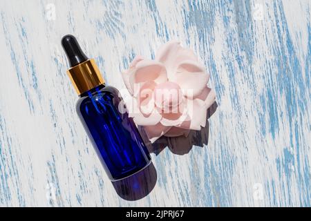 Sérum ou liquide cosmétique, huile sur fond bleu en bois avec fleur de rose. Concept pour les cosmétiques naturels, non testé sur les animaux. Ingrédients naturels. Banque D'Images