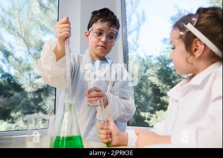 Les enfants font des expériences chimiques, analysent et mélangent du liquide dans des flacons et des tubes à essai en classe au laboratoire scolaire Banque D'Images